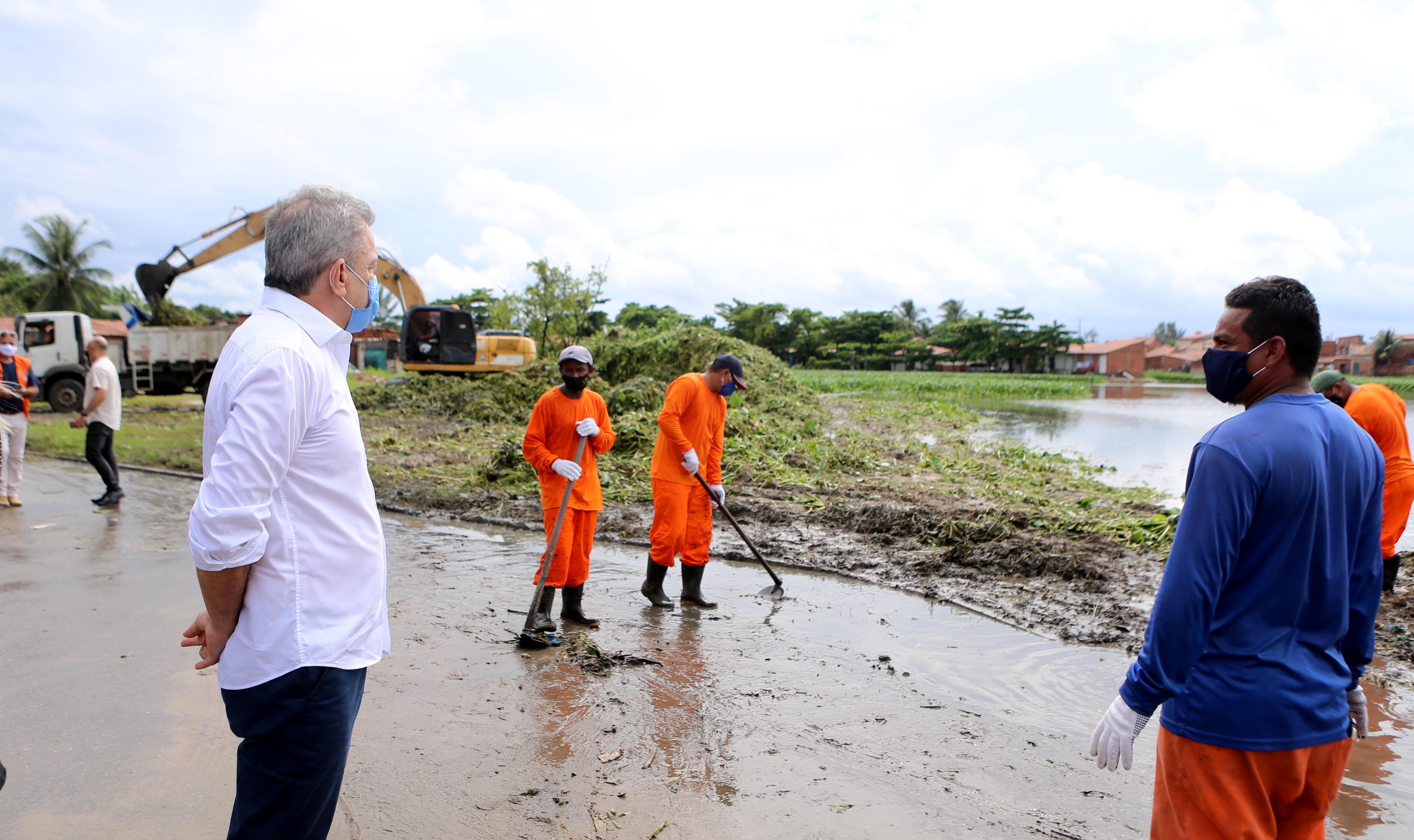prefeito sarto observa homens executando serviço de limpeza numa lagoa